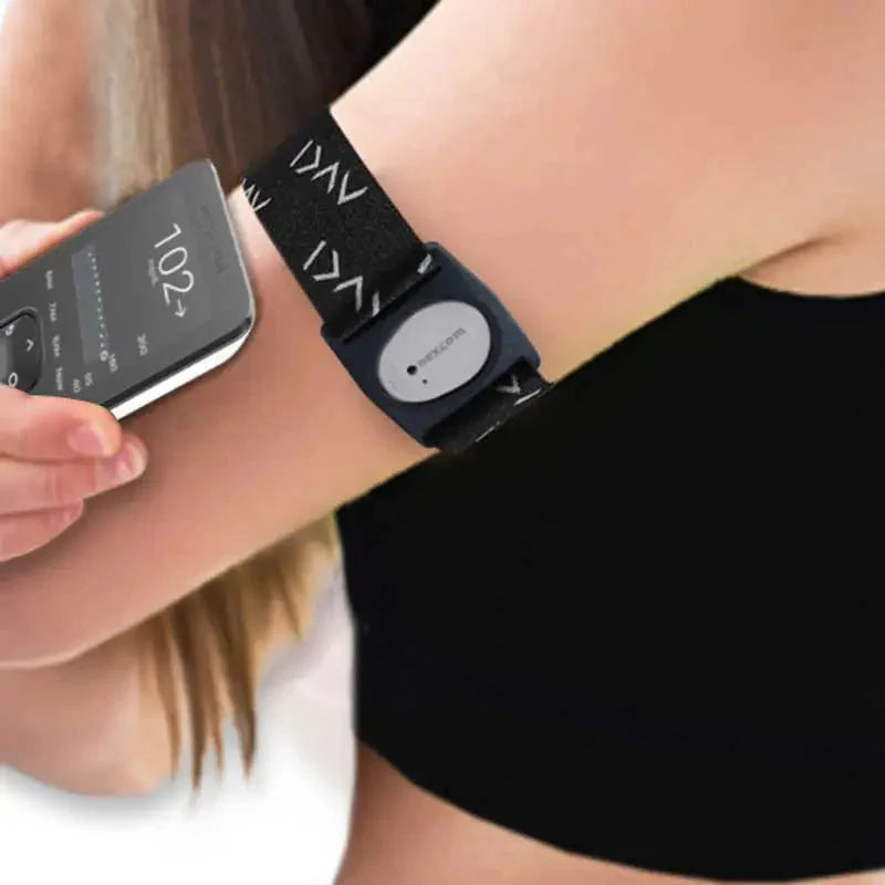 Person wearing a Dexcom G7 armband with a continuous glucose monitor attached, holding a smartphone displaying glucose level data, representing a wearable device for diabetes management. Bild