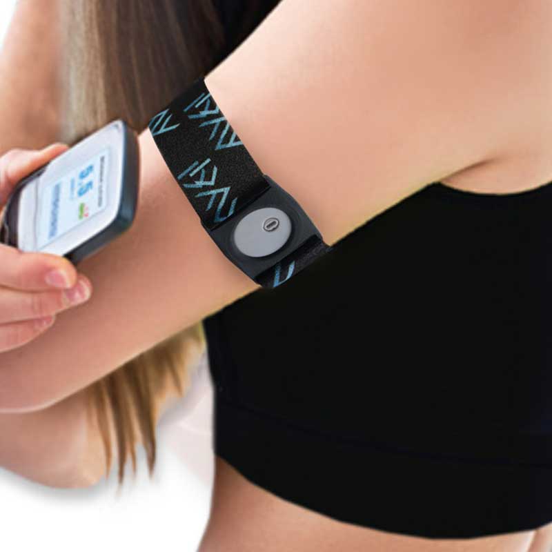 Person wearing a Freestyle Libre 3 armband on their upper arm, holding the glucose monitor to check levels. The black armband with blue patterns provides a snug fit for sports and activities. Bild