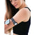 A woman using a smartphone app while wearing a Freestyle Libre 2 Armband with a patterned strap on her upper arm. The armband securely holds the sensor.